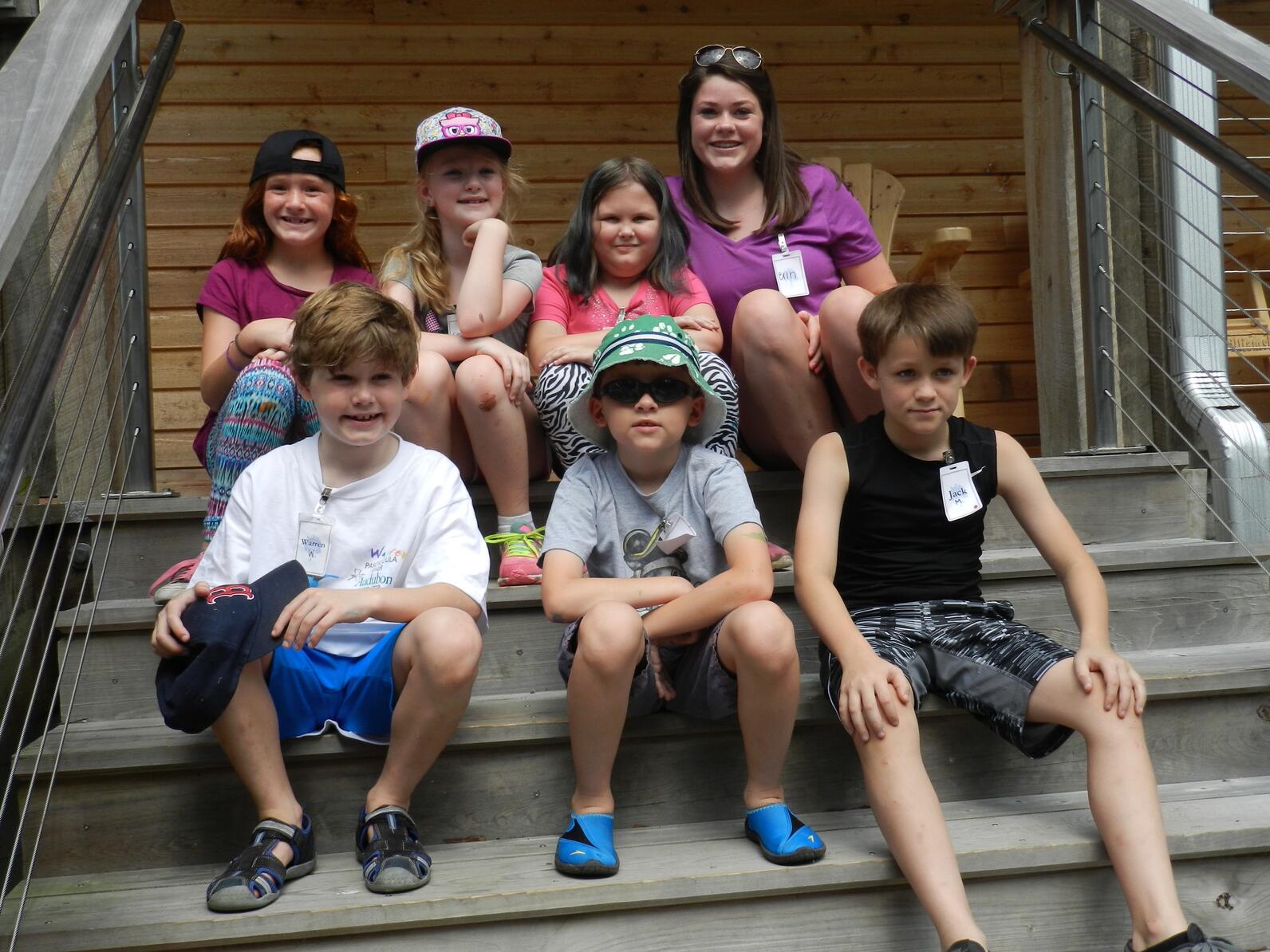 Six children and one woman sit in two rows on a set of stairs.