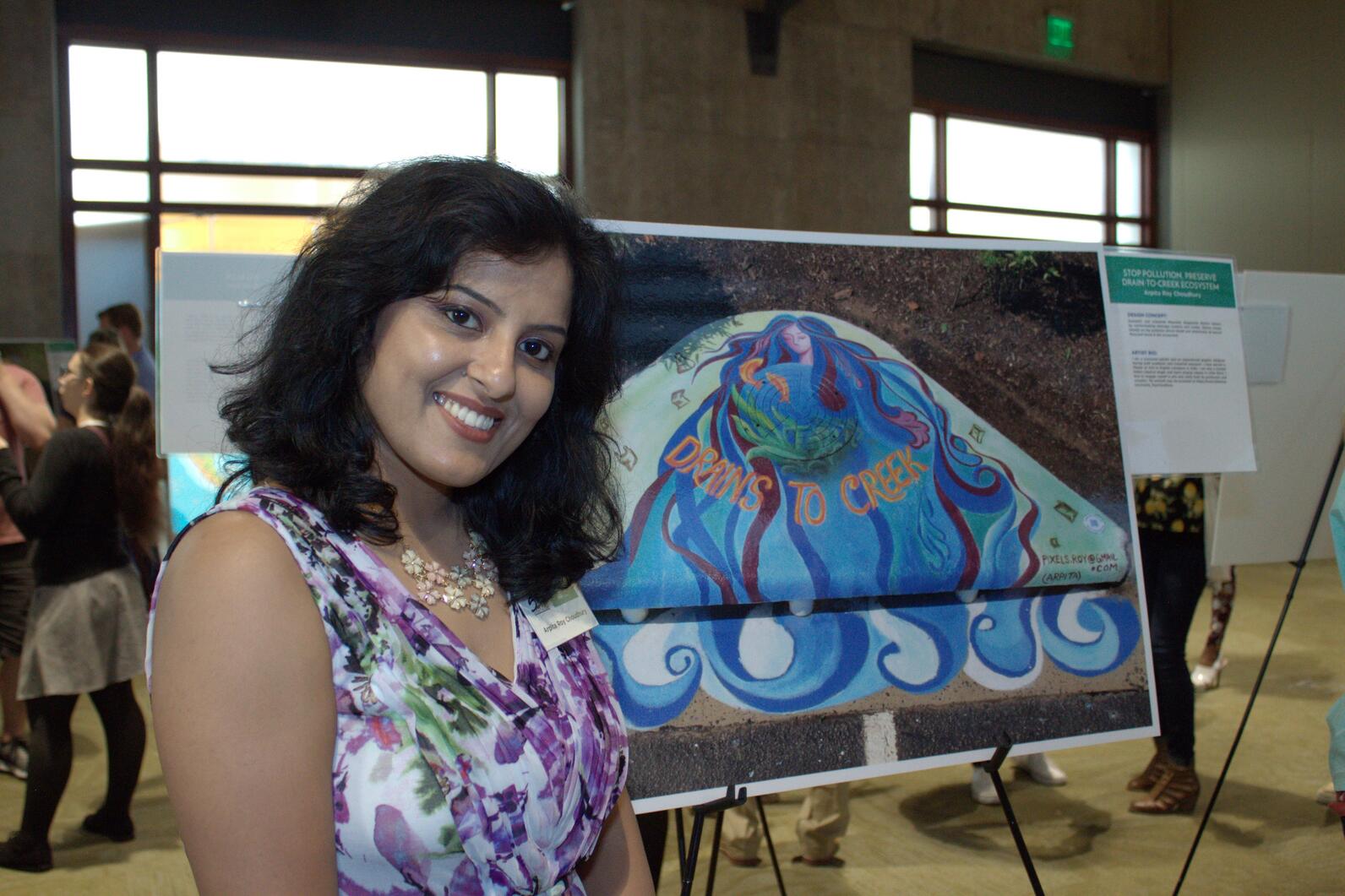 A woman stands in a gallery next to artwork with text that reads, drains to creek.