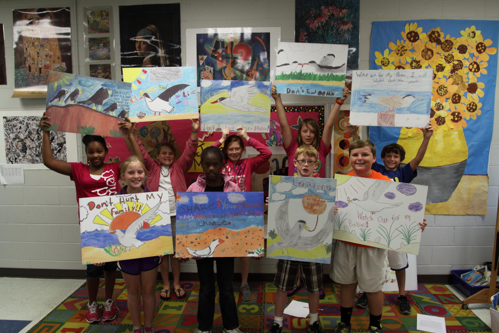 Nine kids hold up their artwork with various messages to protect birds.